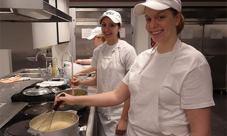 Culinary Dietetics students stir food in pots in the kitchen lab