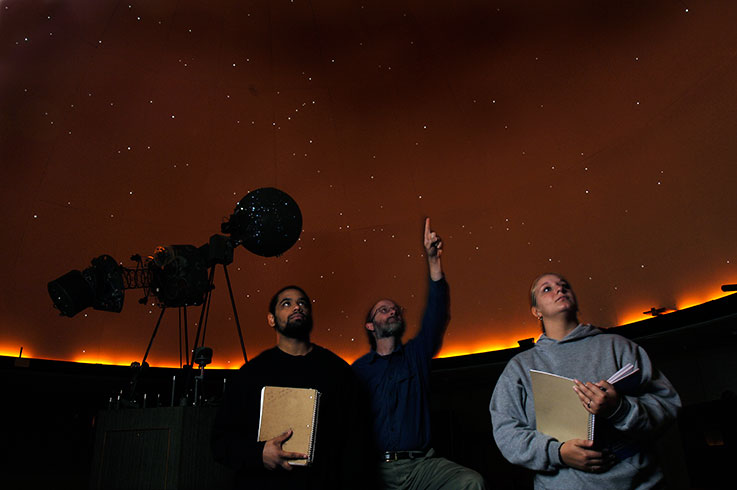 Three people in the IUP Planetarium looking up and pointing at stellar images