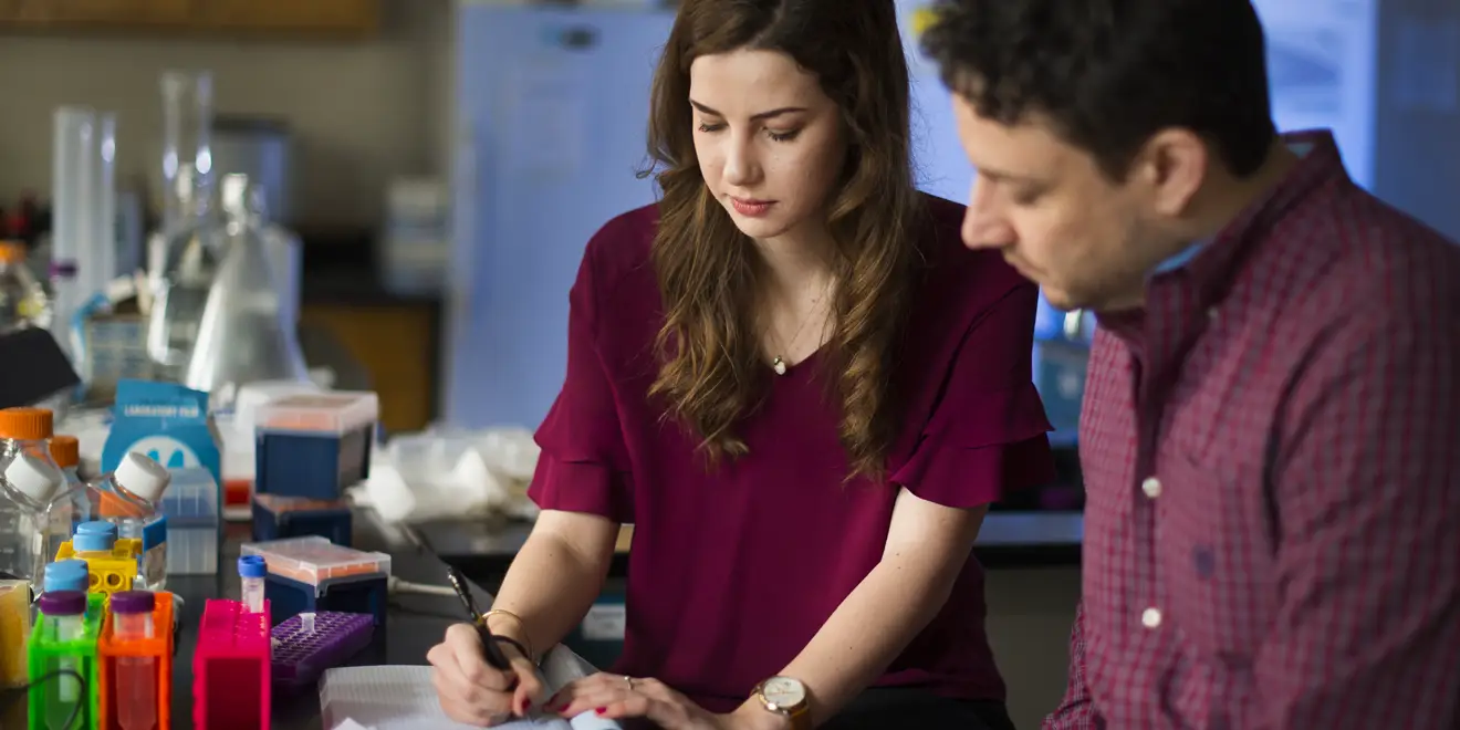 Two people in a science lab recording notes in a tablet