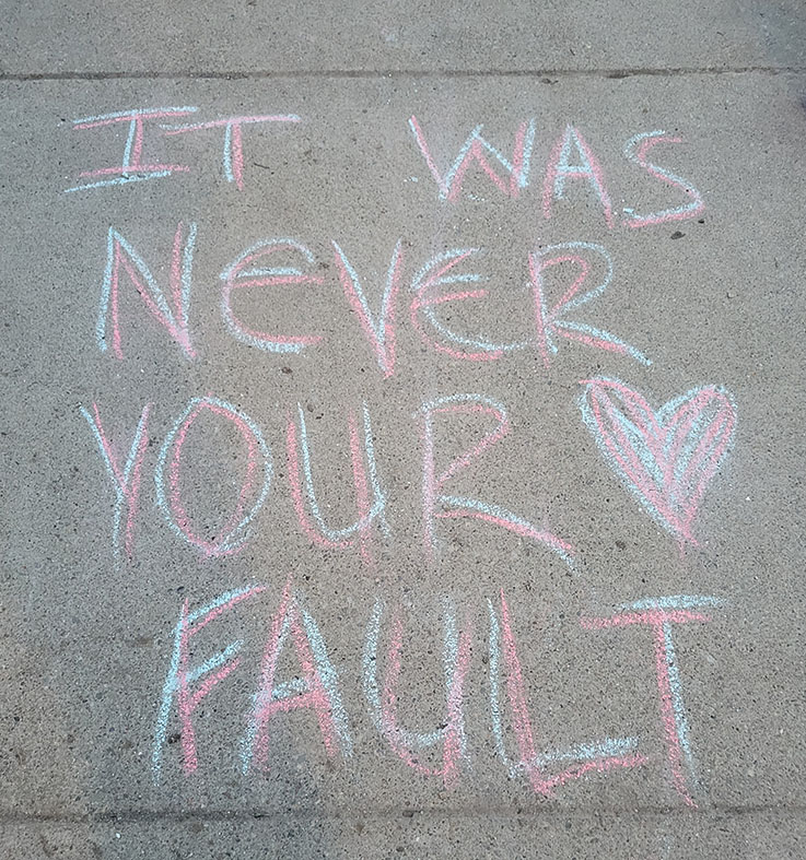 image of chalked message on the sidewalk that says "It was never your fault"