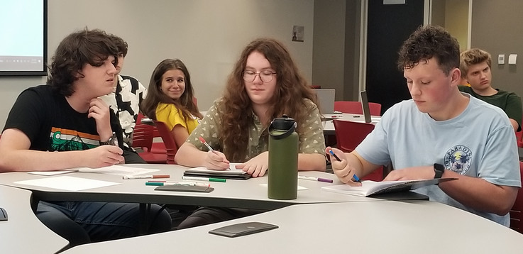 Three students sit at a table and work on their assignment in Prof. Sell's session.