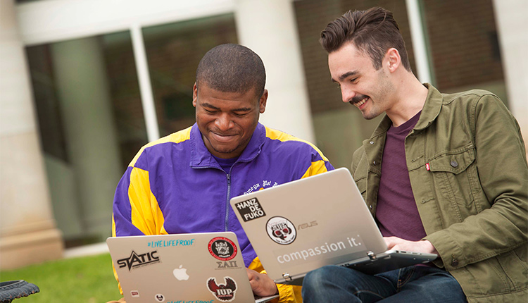 Two honors college male students looking down at a laptop