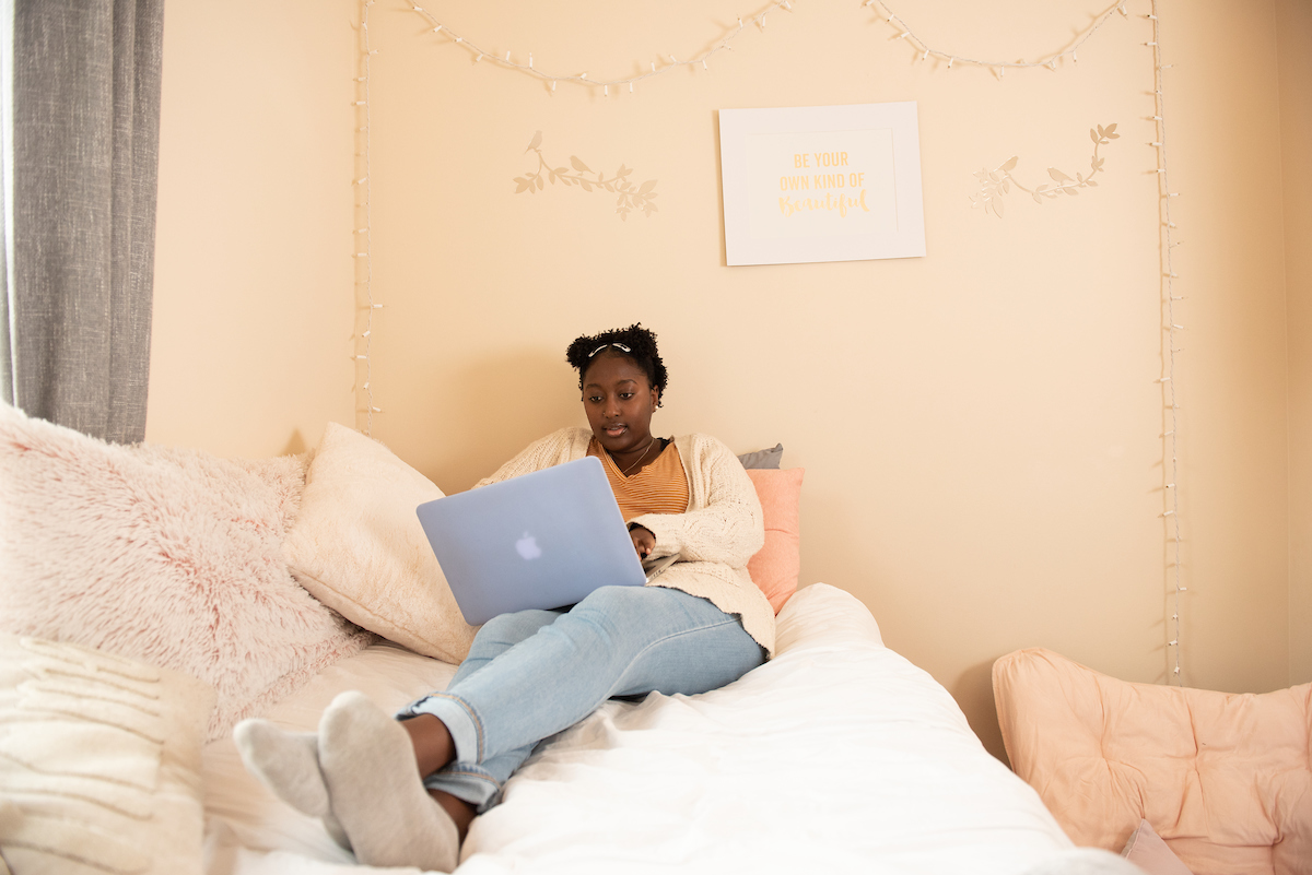 An IUP student does some work on her laptop as she sits on the bed in her private suite.