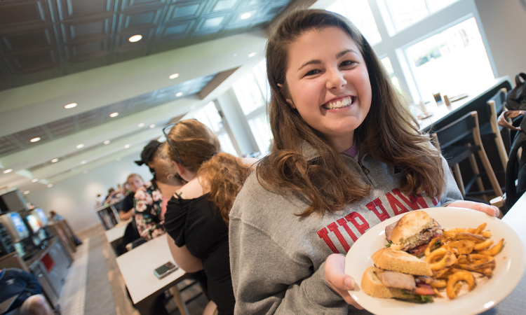 A smiling student holds a plate of food in the dining hall.