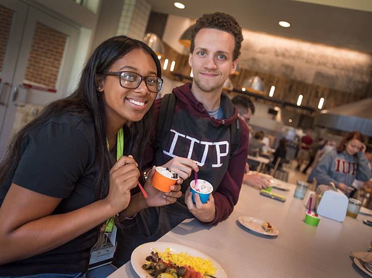 Two smiling students eat together in an IUP dining hall.