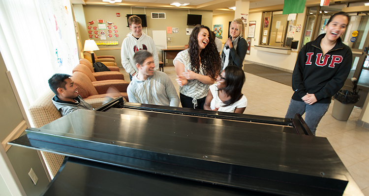 Students laugh around a piano while hanging out in Putt Hall