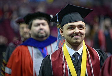 a smiling student at a graduation ceremony in cap and gown