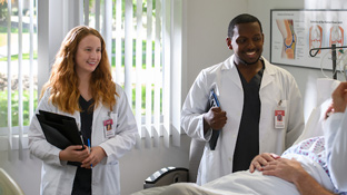 Two nursing students talk to a patient in a hospital bed