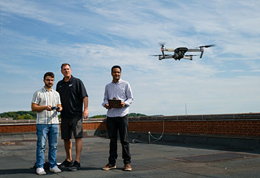 three people standing on a rooftop controlling a drone