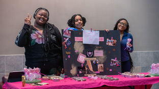 Three students posing at a Valentine's Day-themed table with various wrapped candy for sale