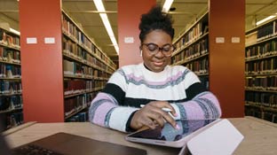 A student sitting in a library studying from a book