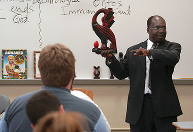 a professor standing in front of a class holding a red statue