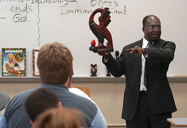 a professor standing in front of a class holding a red statue
