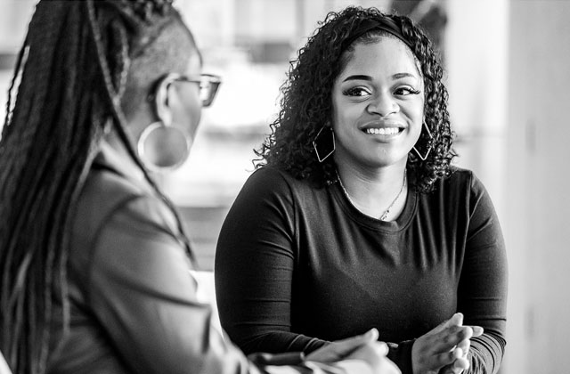 a black and white photo of two women sitting at a table talking