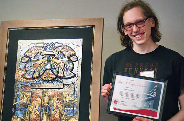 a smiling student holding an award while standing next to stained glass