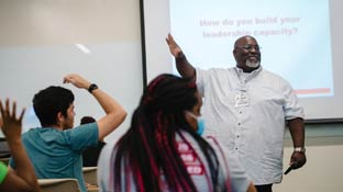 A professor at the front of a class speaking to his students