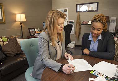 two women sitting at a table looking over papers