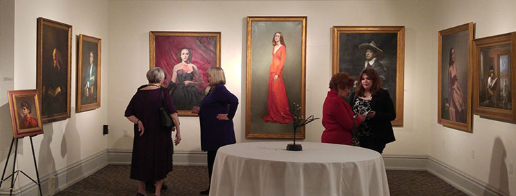 A few people look at paintings hung on the wall of an art gallery