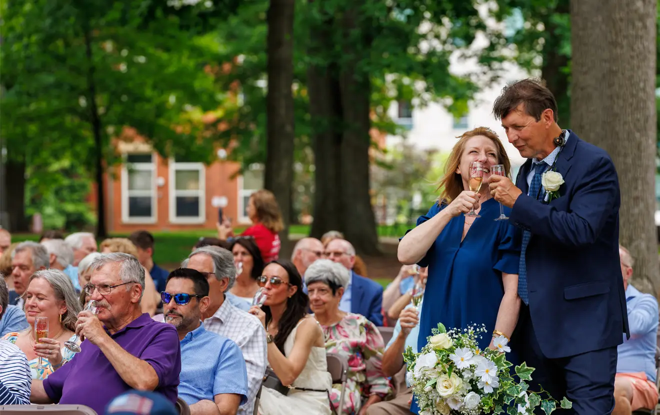Groups of people sitting in the oak grove holding up glasses of champagne.