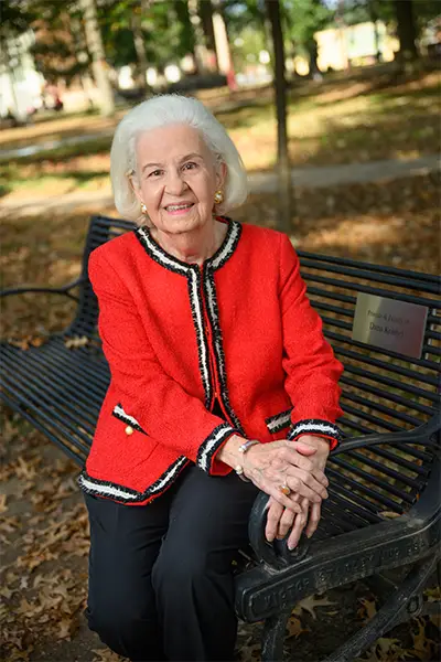 Ruth Riesenman sitting at on a bench in the IUP Oak Grove in the fall