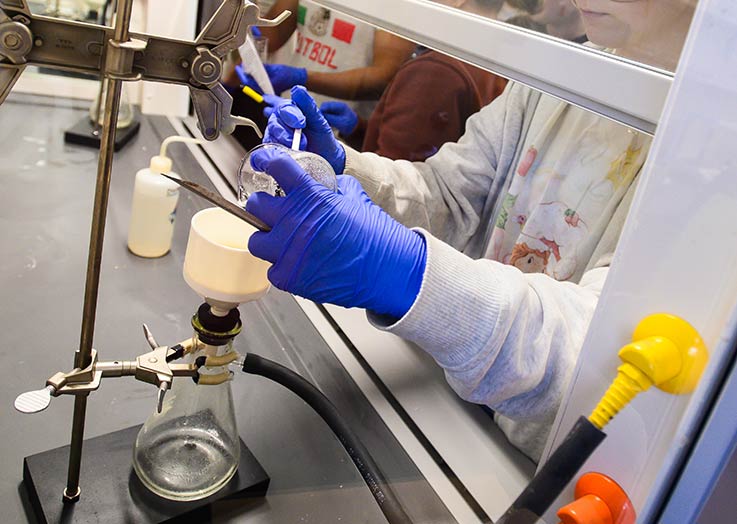  A student with gloved hands working with chemicals in a laboratory classroom