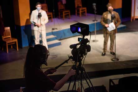 In October, IUP’s Theater-by-the-Grove gave livestreamed performances of Shakespeare’s Much Ado about Nothing, reimagined as a 1940s radio play. In back, from left, Riley Guers (Leonato) and Addison “Addie” Minich (Borachio) performed while Megan Carpenter operated a video camera. (Brian Henry) Photo of a theater during a production