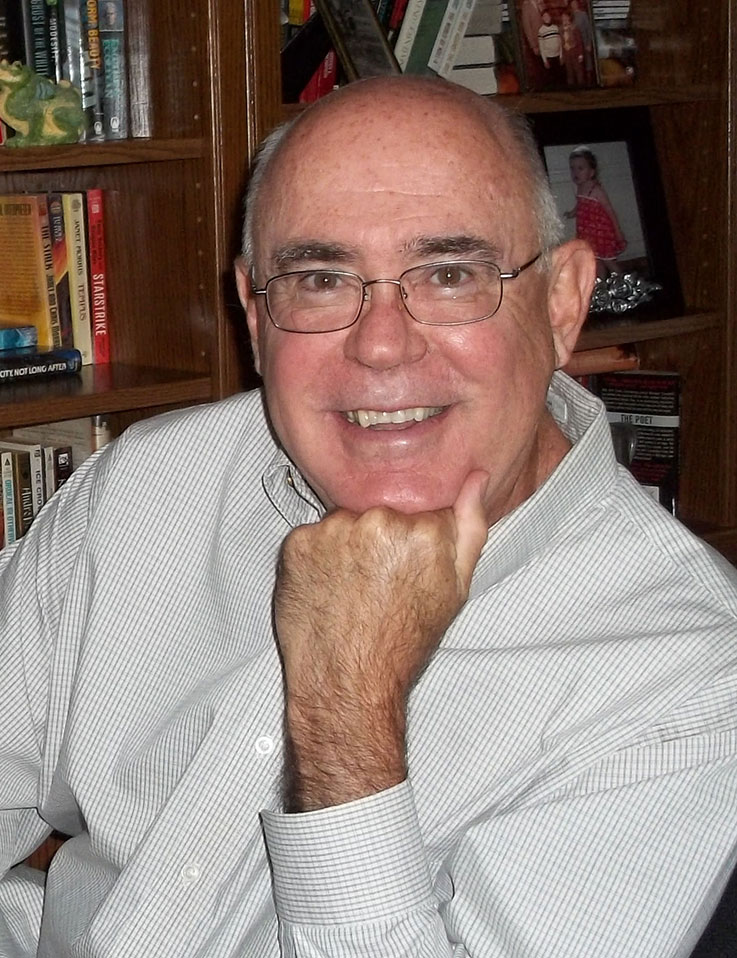 Portrait of William Bentrim with his chin resting on his hand, with bookshelves with books and children’s photographs behind him