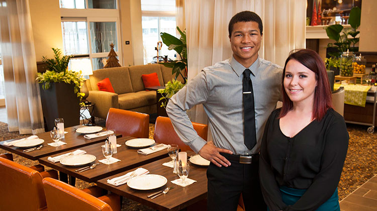 Two Hospitality students in a dining area set for guests.