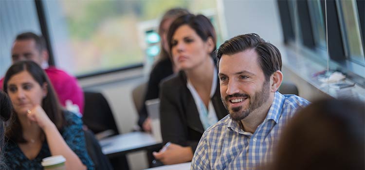 In an MBA classroom, a student smiles as he looks towards the front of the room.