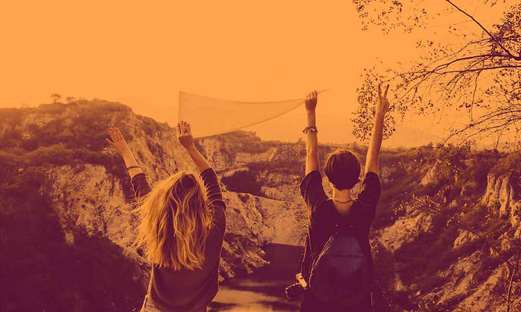 two students looking over a cliff with their hands raised