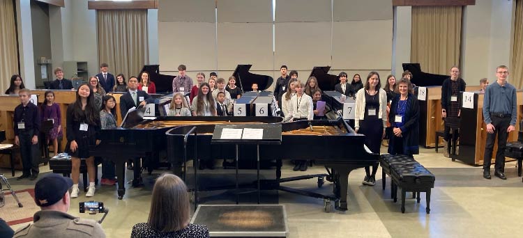 Students and faculty surrounded by many pianos at the 2024 Piano Monster Concert