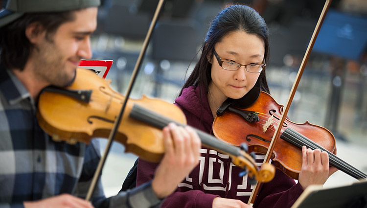 Two students play violins or violas in a rehearsal.
