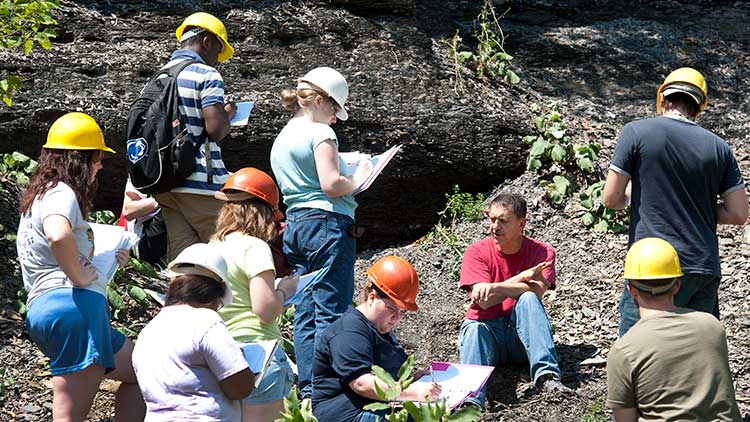 Students wearing hard hats taking notes while working in the field