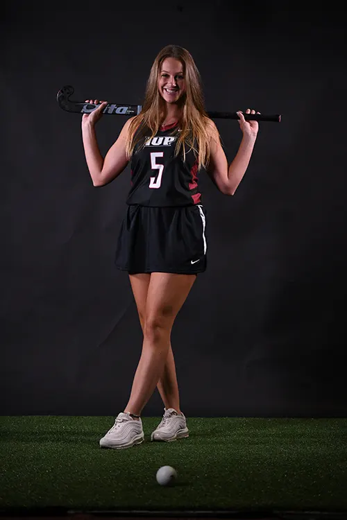 Riley Yonchiuk facing the camera with her field hockey stick resting on her shoulders