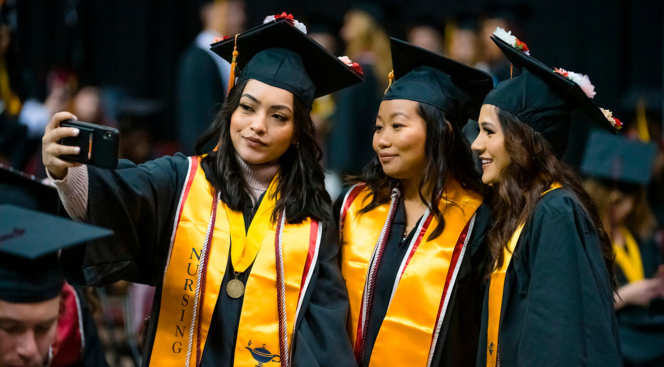 Graduating students in cap and gown posing for a selfie