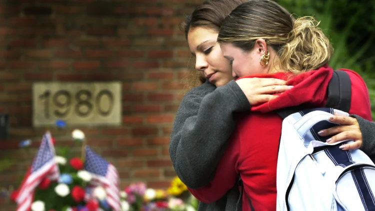 Two students hugging next to a grouping of flowers placed to remember those lost on 9/11