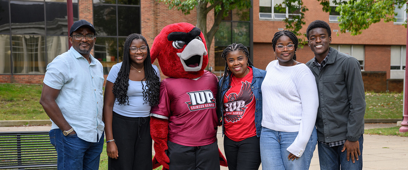 A family smiles for a photo with Norm in the Oak Grove on Family Weekend. 