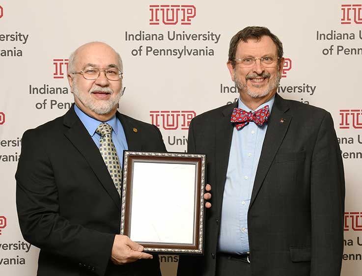 White IUP logo sitting on top of a red wood grain background