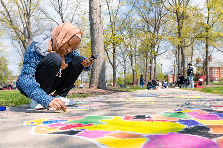 A student sitting on the sidewalk and drawing with chalk