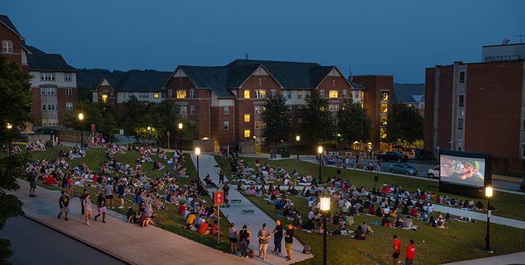 Students sitting on Foster Lawn in the evening watching a movie on an outdoor screen