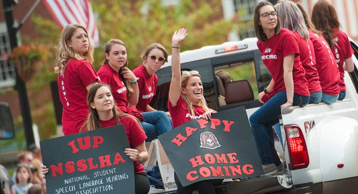 A group of students wave with signs during the IUP Homecoming parade