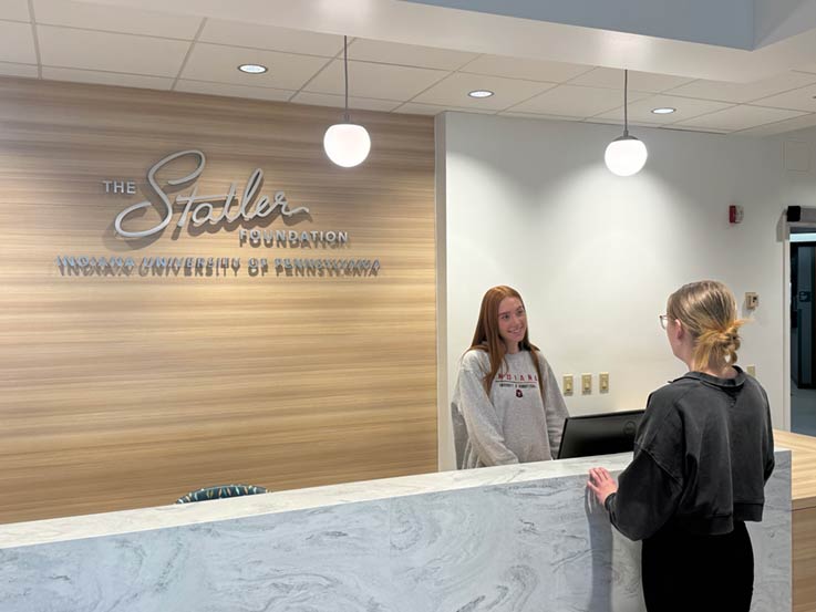 Hotel, Restaurant, Tourism, and Event Management students Riley Rehrig, behind desk, with Jade Peffer in front of the Statler Foundation’s simulation lab front desk