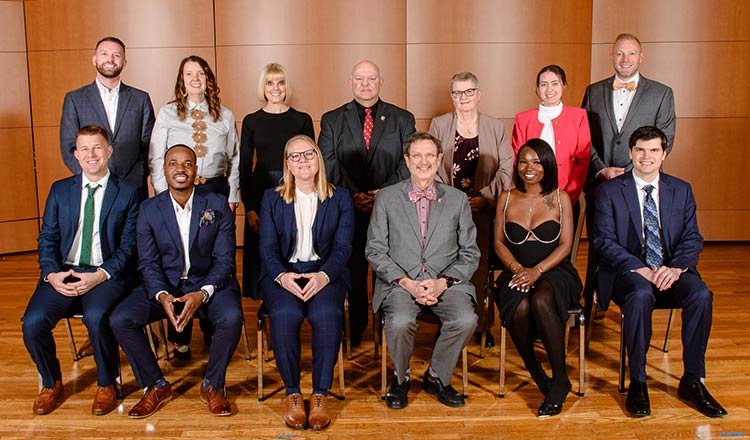 The five 2025 recipients of the IUP Young Adult Achievement Award seated on stage with IUP President Driscoll. Standing behind them are seven previous winners of the award.