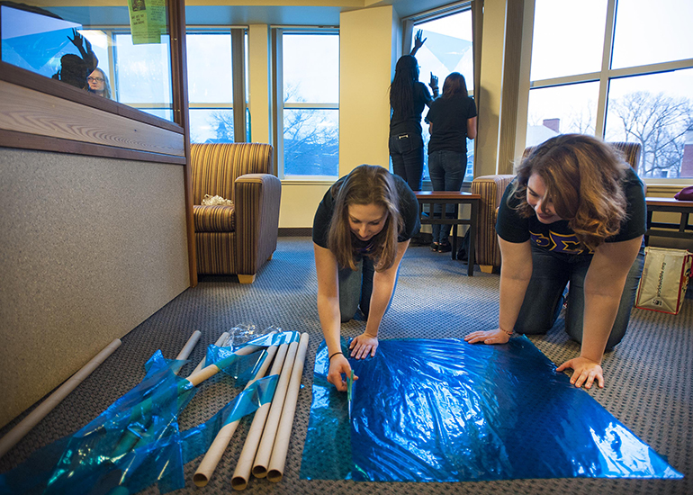 Members of Phi Sigma Pi attach blue cellophane to residence hall windows