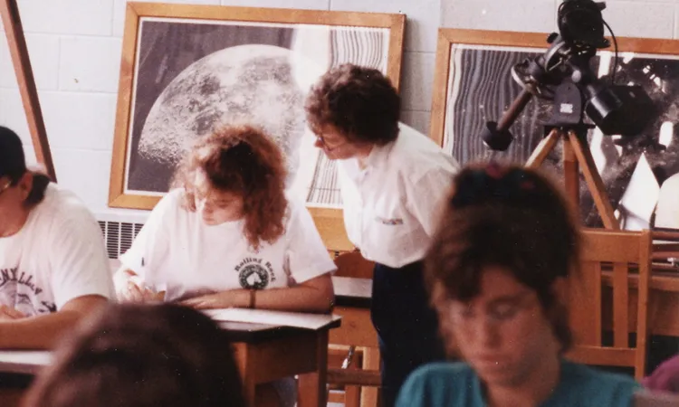 a teacher looks over the shoulder of a student writing at their desk