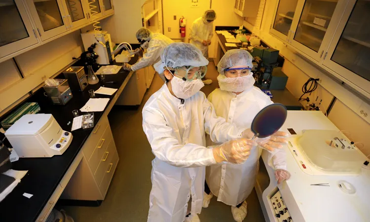 two people in lab coats, face masks, and hair covers working in a lab