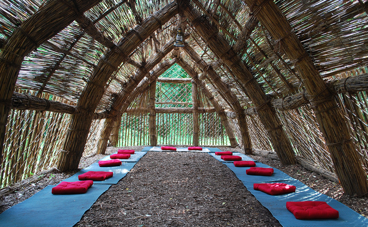 The interior of a completed structure made of reed grasses, with mats lining the edges of the mulched floor and pillows placed on top of the mats for seating