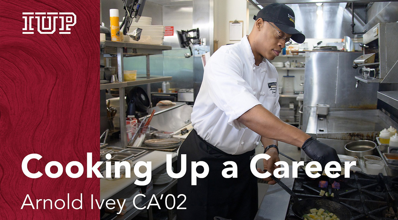 A chef in a white coat and black hat working over a gas stove in a commercial style kitchen.  The words "Cooking Up a Career: Arnold Ivey CA'02" are displayed over the image