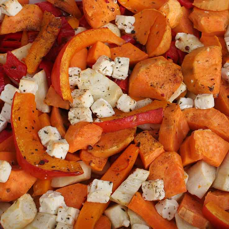 A cooked casserole that includes mostly chopped pieces of pumpkin, with some slices of red peppers and some small, diced pieces of chicken and potatoes.