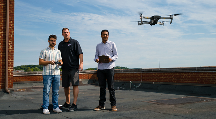 three people on a roof flying a drone